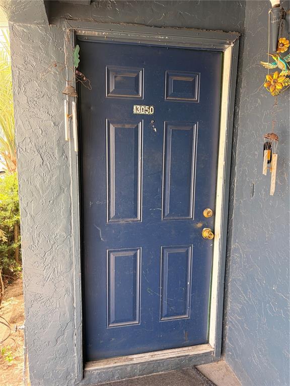 A dark blue front door with four panels and a gold knob is set in a wall — 13050 LONDONDARY PLACE, TAMPA, FL