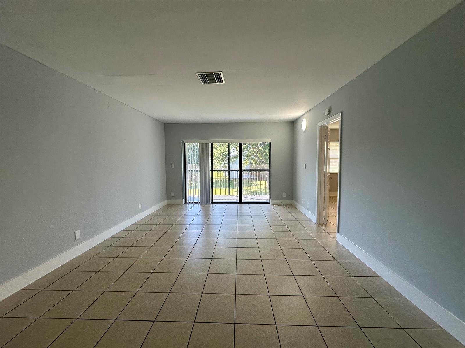 An empty living room with light gray walls, tiled flooring, and a sliding glass door — 4773 Arjaro Drive, West Palm Beach FL 33407, WEST PALM BEACH, FL