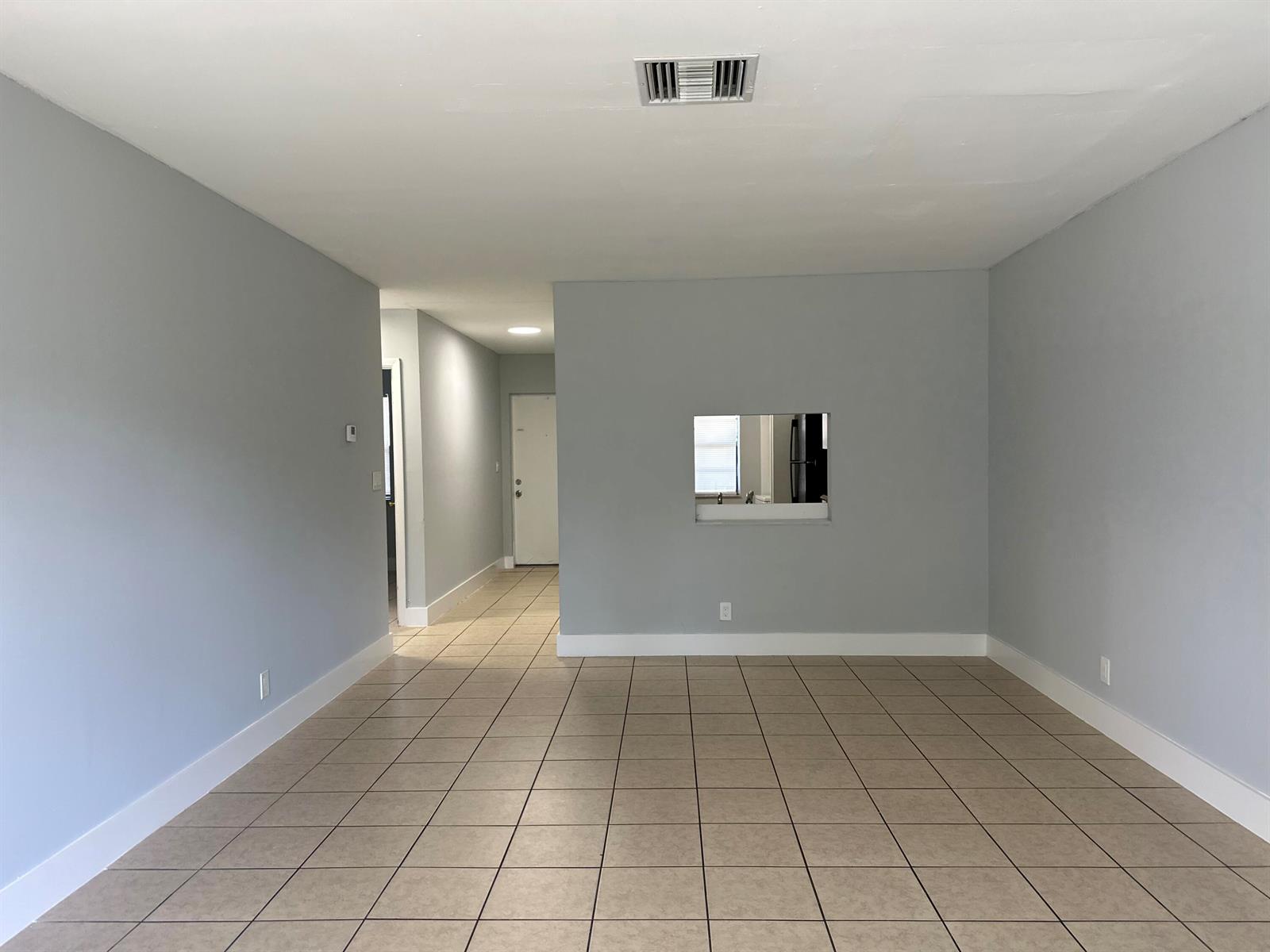 An empty room with light gray walls, tan tile flooring, and a kitchen pass-through window — 4773 Arjaro Drive, West Palm Beach FL 33407, WEST PALM BEACH, FL