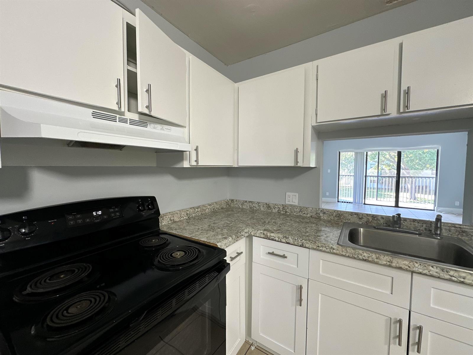 A kitchen features white cabinets, granite-look countertops, a black electric stove, and a stainless sink — 4773 Arjaro Drive, West Palm Beach FL 33407, WEST PALM BEACH, FL