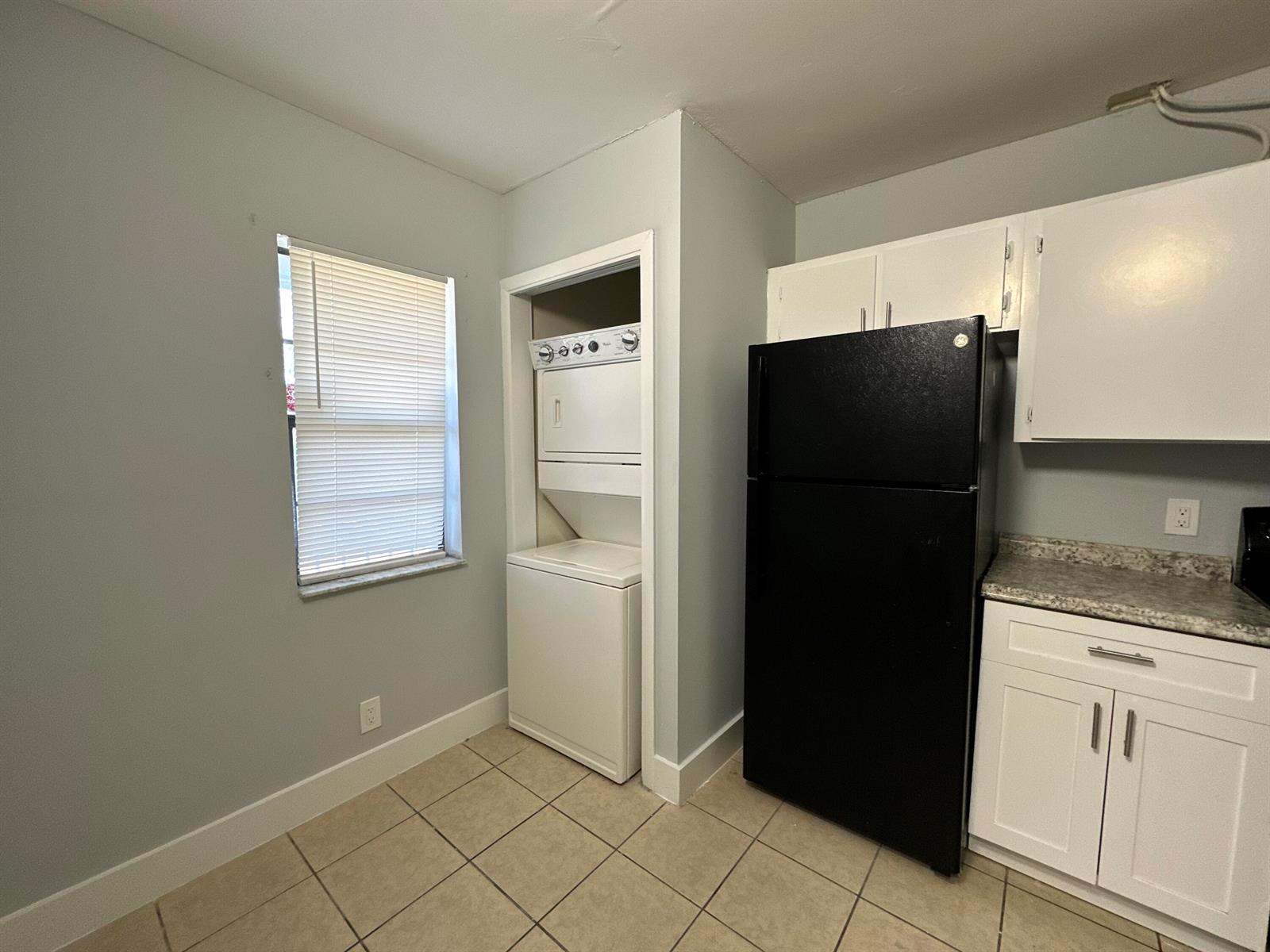 A kitchen features a stackable washer and dryer, a black refrigerator, and white cabinets — 4773 Arjaro Drive, West Palm Beach FL 33407, WEST PALM BEACH, FL