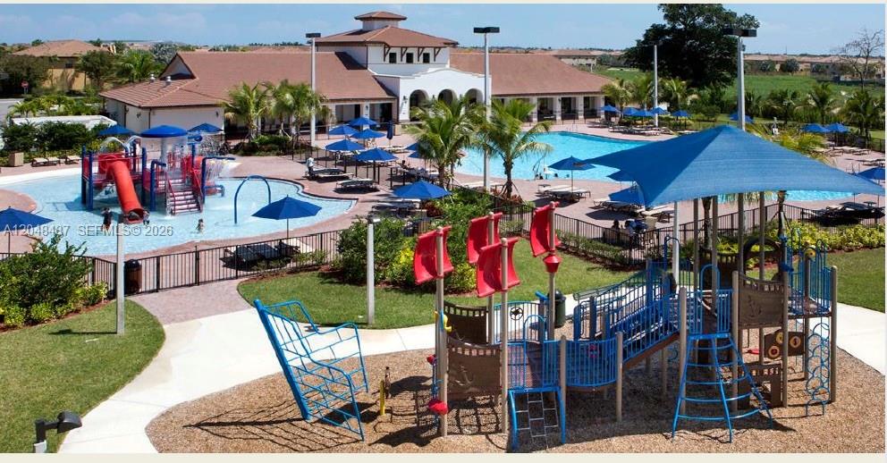 An outdoor playground with a blue shade structure sits beside a swimming pool and clubhouse — HOMESTEAD, FL
