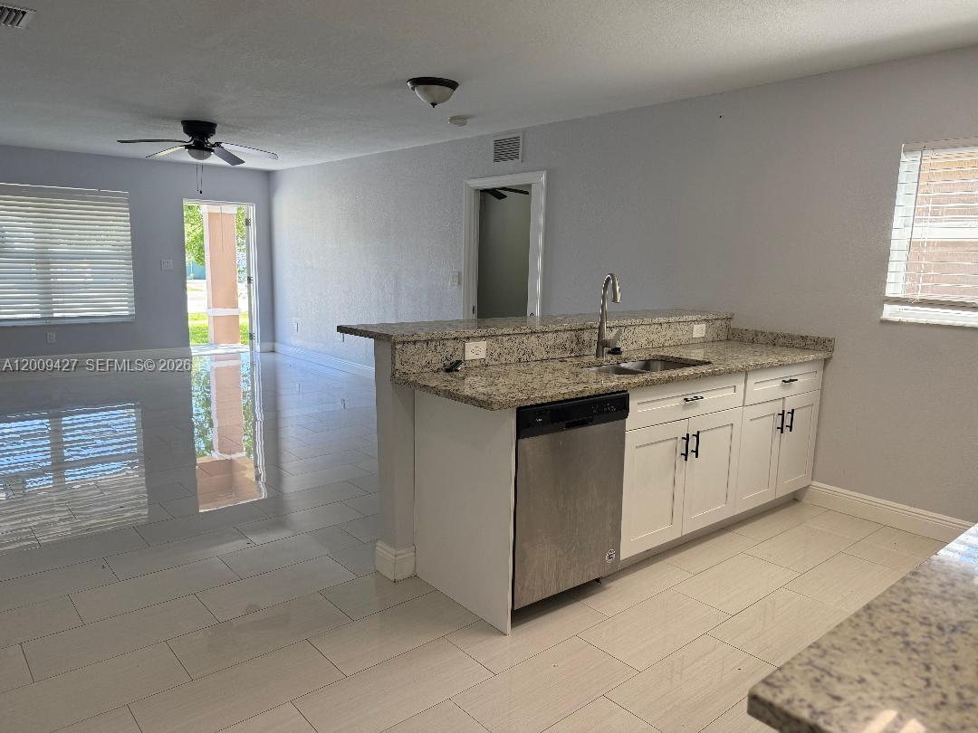 A kitchen with granite countertops, white cabinets, and a stainless steel dishwasher overlooks a living area — 2713 NW 6th St, Pompano Beach FL 33069, POMPANO BEACH, FL