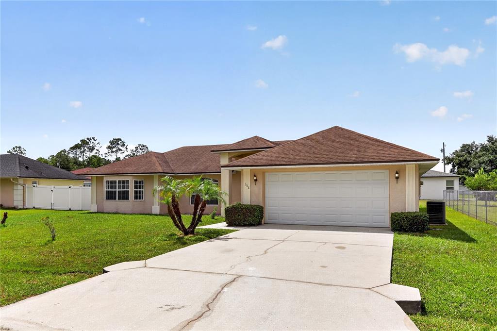 A single-story house with a two-car garage and a concrete driveway under a blue sky — 308 CLERMONT DRIVE, KISSIMMEE, FL