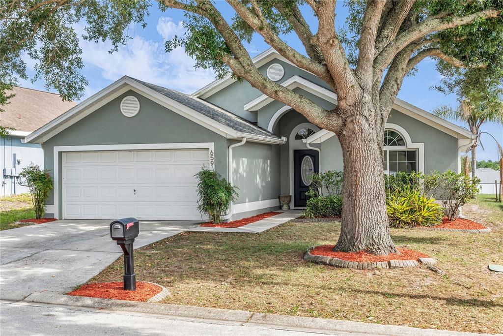 A single-story house with a two-car garage, a large tree, and a front entryway — 659 RESTON PLACE, DAVENPORT, FL