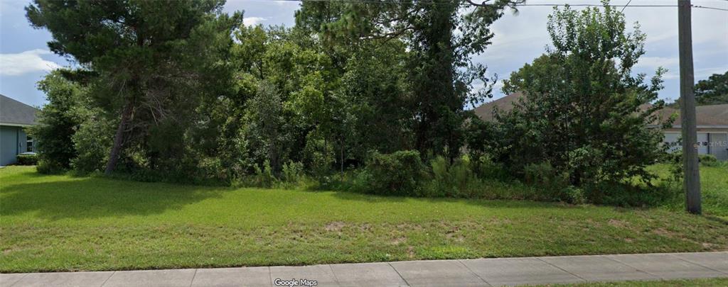 A vacant, tree-covered residential lot is situated between two existing houses along a sidewalk — 14144 SPRING HILL DRIVE, SPRING HILL, FL