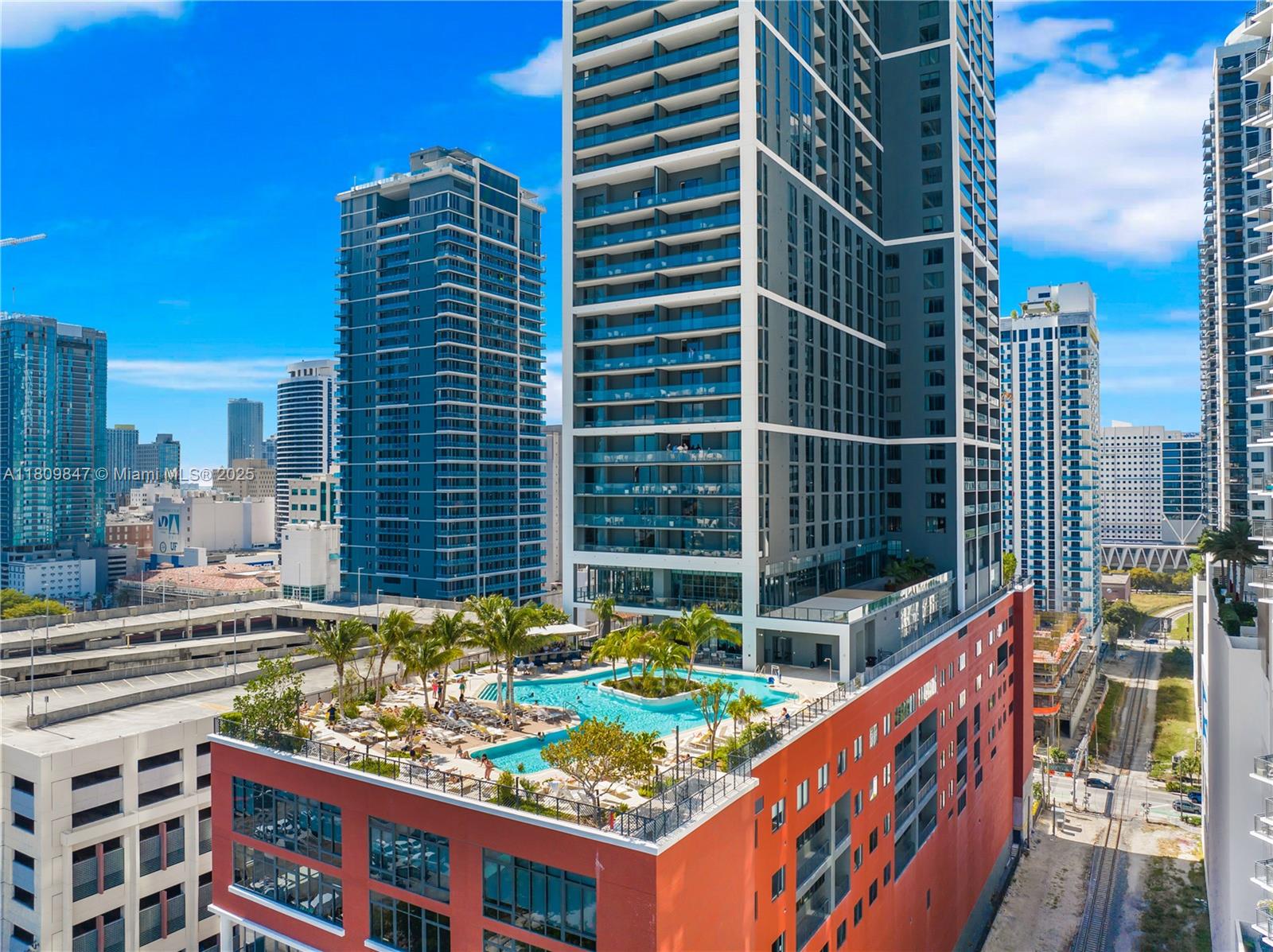 An elevated view of a high-rise building featuring a rooftop swimming pool and palm trees — 159 NE 6th St # 3005, Miami FL 33132, MIAMI, FL