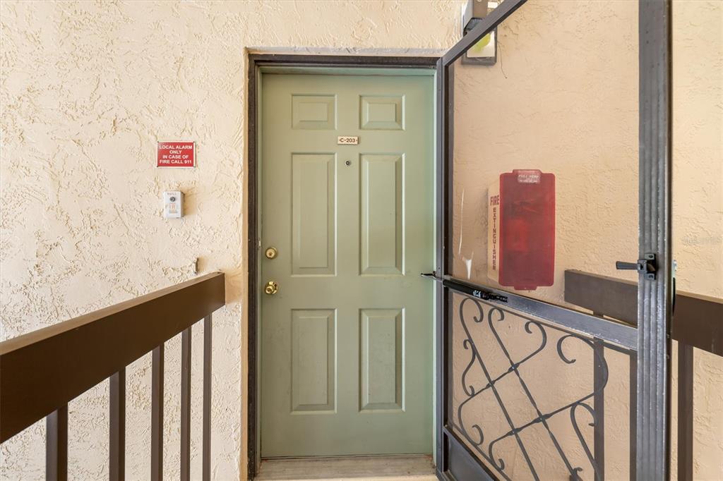 A light green apartment door with a screen door and fire safety equipment nearby — 19505 QUESADA AVENUE UNIT C203, PORT CHARLOTTE, FL