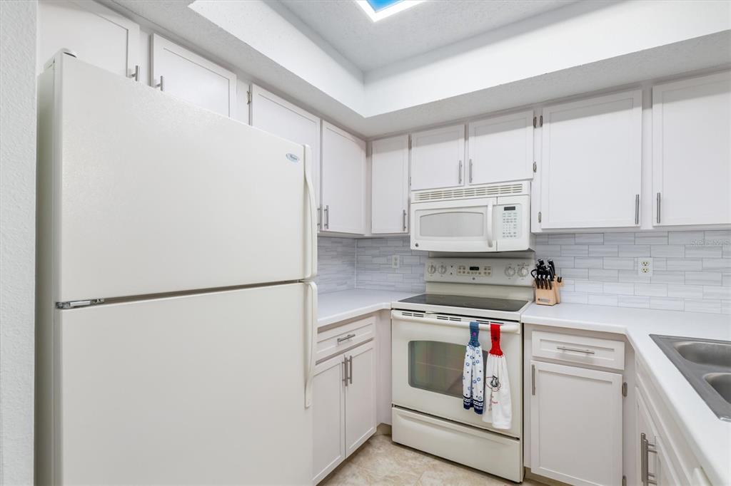 A kitchen with white cabinets, white appliances, and a light-colored tile backsplash — 19505 QUESADA AVENUE UNIT C203, PORT CHARLOTTE, FL