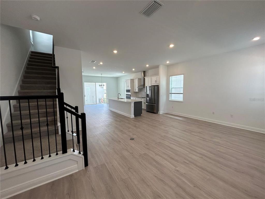 An open-concept living area features a staircase, kitchen with an island, and light wood flooring — 16902 HAMLIN OASIS LOOP, WINTER GARDEN, FL