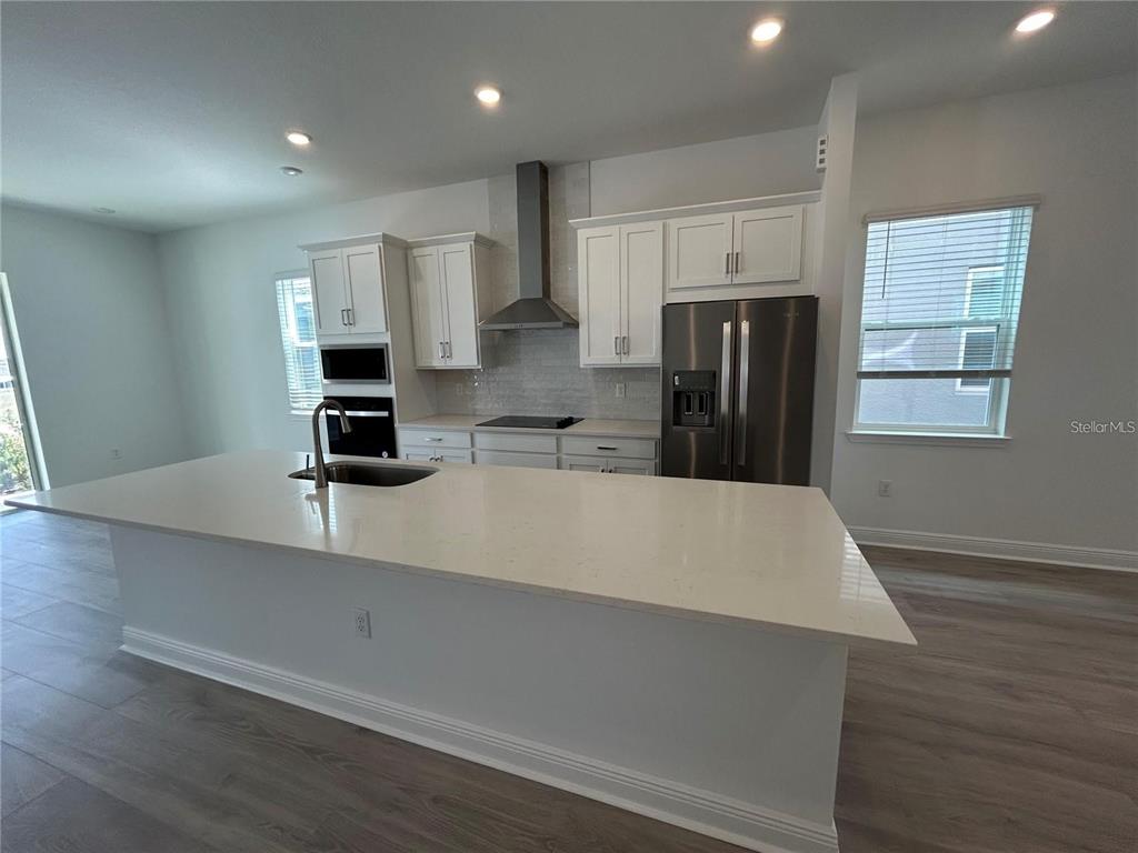 A modern kitchen features white cabinets, stainless steel appliances, and a large quartz-topped island — 16902 HAMLIN OASIS LOOP, WINTER GARDEN, FL