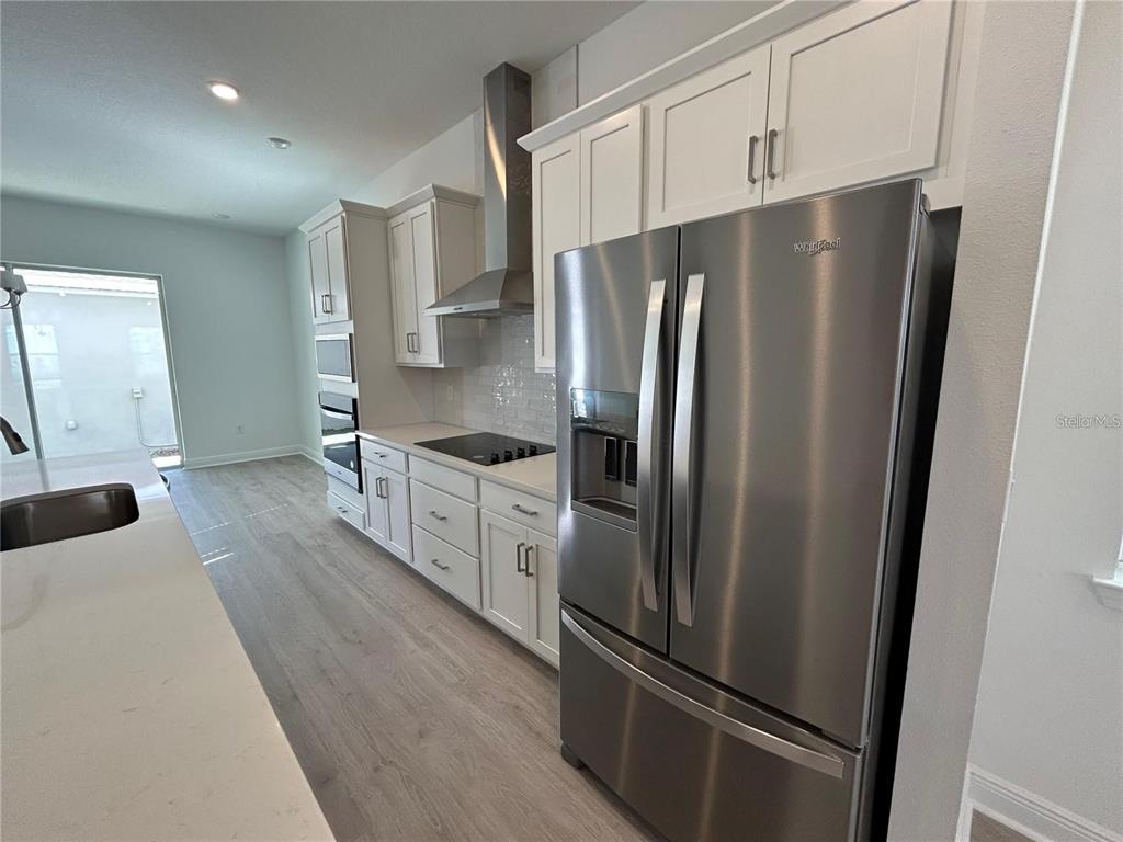 A modern kitchen features white cabinets, stainless steel appliances, and light wood-look flooring — 16902 HAMLIN OASIS LOOP, WINTER GARDEN, FL