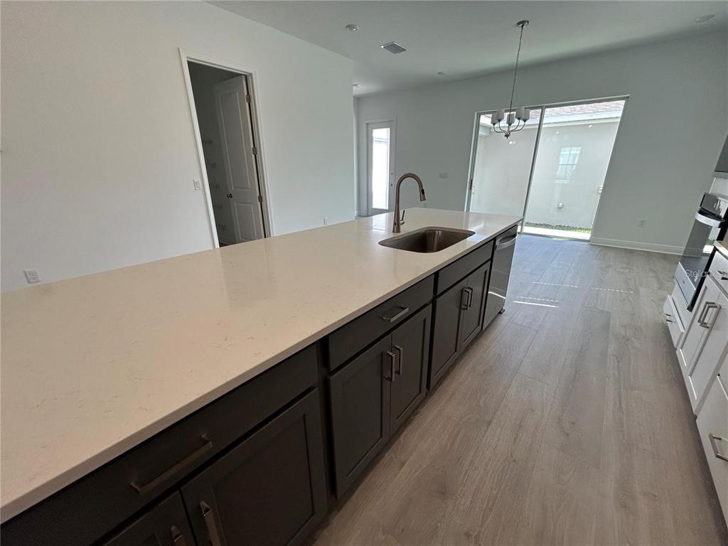 A kitchen island with dark cabinets and a light countertop sits in an open-concept room — 16902 HAMLIN OASIS LOOP, WINTER GARDEN, FL