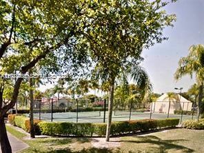 A fenced tennis court surrounded by trees and landscaping in a residential area — 901 Lyons Rd # 1208, Coconut Creek FL 33063, COCONUT CREEK, FL