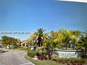 A paved driveway leads to a landscaped entrance sign for Coco Parc with palm trees — 901 Lyons Rd # 1208, Coconut Creek FL 33063, COCONUT CREEK, FL