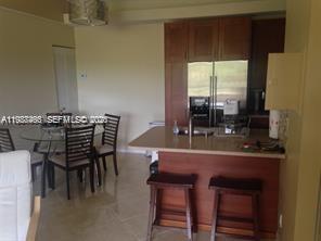 A kitchen with wooden cabinets and a breakfast bar sits next to a glass dining table — 901 Lyons Rd # 1208, Coconut Creek FL 33063, COCONUT CREEK, FL