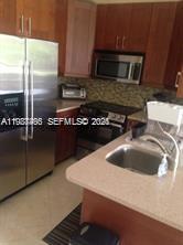 A kitchen features stainless steel appliances, wood cabinets, a tiled backsplash, and a light-colored countertop — 901 Lyons Rd # 1208, Coconut Creek FL 33063, COCONUT CREEK, FL