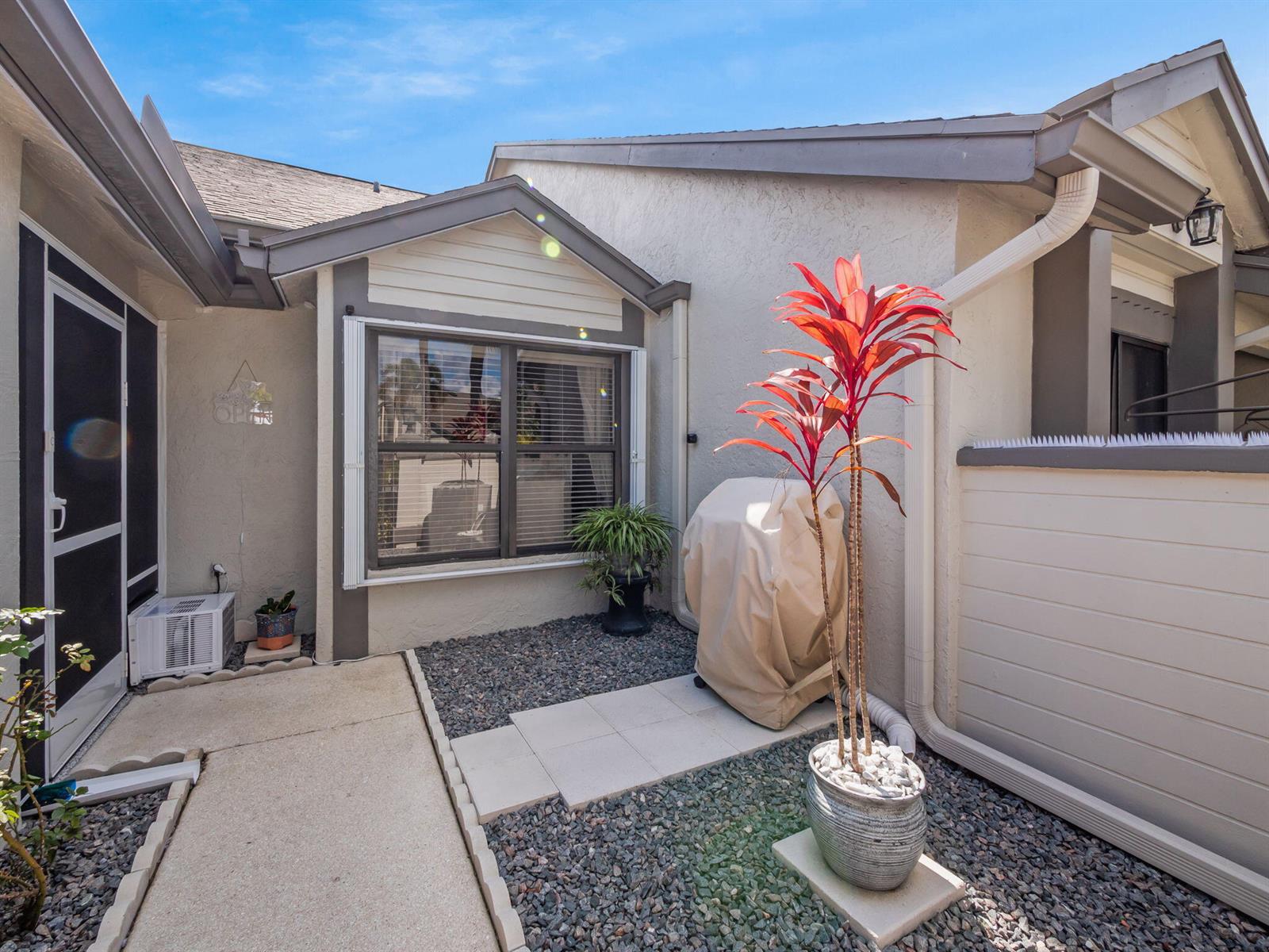 A small patio area features a concrete walkway, gravel landscaping, a potted plant, and grill — 1103 Landings Boulevard, FL 33413, FL