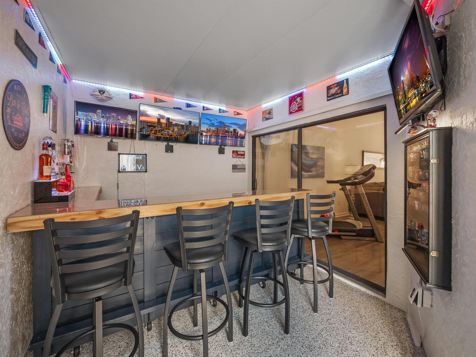A home bar area features a wooden counter, four black stools, and multiple wall-mounted televisions — 1103 Landings Boulevard, FL 33413, FL