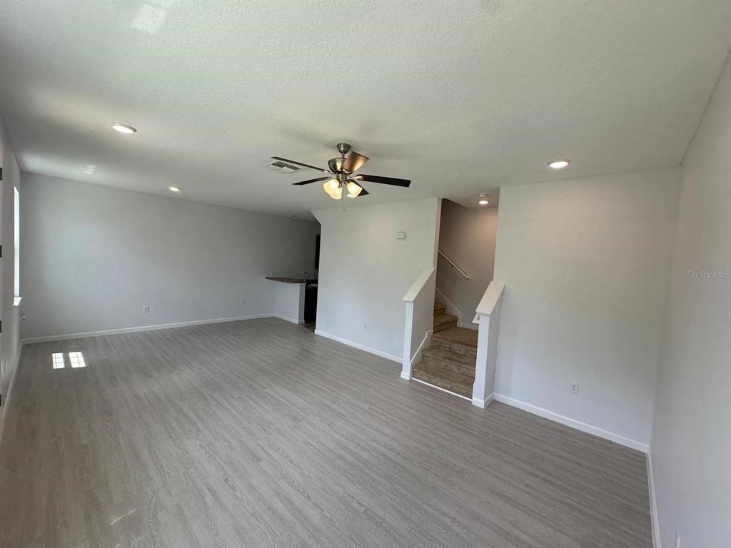 A living room with light wood-look flooring, a ceiling fan, and stairs leading upward — 112 HOLLY VILLAGE DRIVE, DAVENPORT, FL
