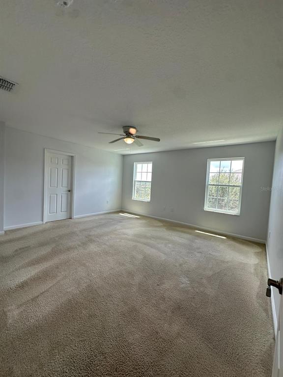 An empty bedroom features beige wall-to-wall carpeting, white walls, two windows, and a ceiling fan — 112 HOLLY VILLAGE DRIVE, DAVENPORT, FL