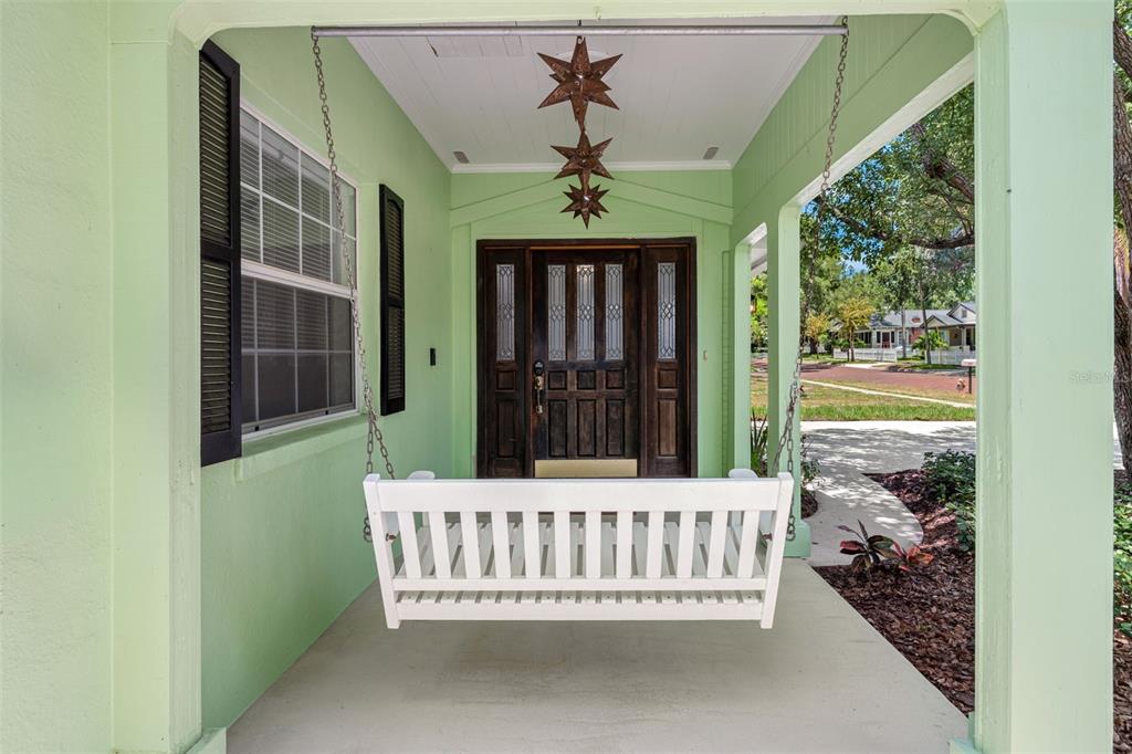 A light green front porch features a white hanging swing and a dark wooden door — 641 WILKIE STREET, DUNEDIN, FL