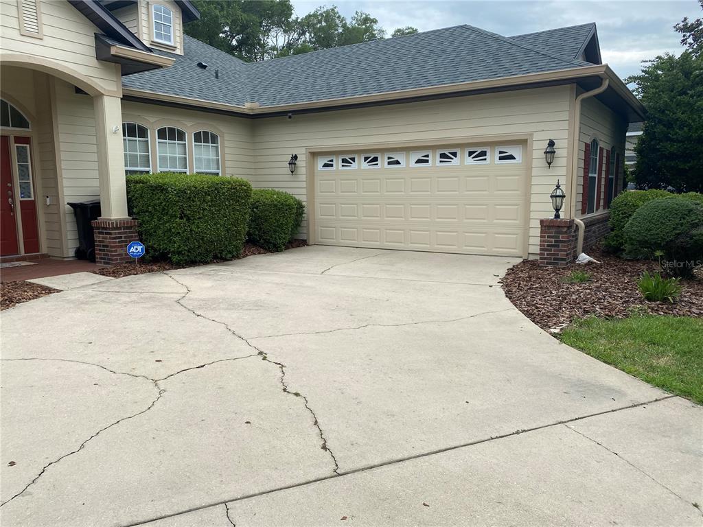 A beige house features a two-car garage, a concrete driveway with cracks, and landscaping — 8389 SW 80TH PLACE, GAINESVILLE, FL