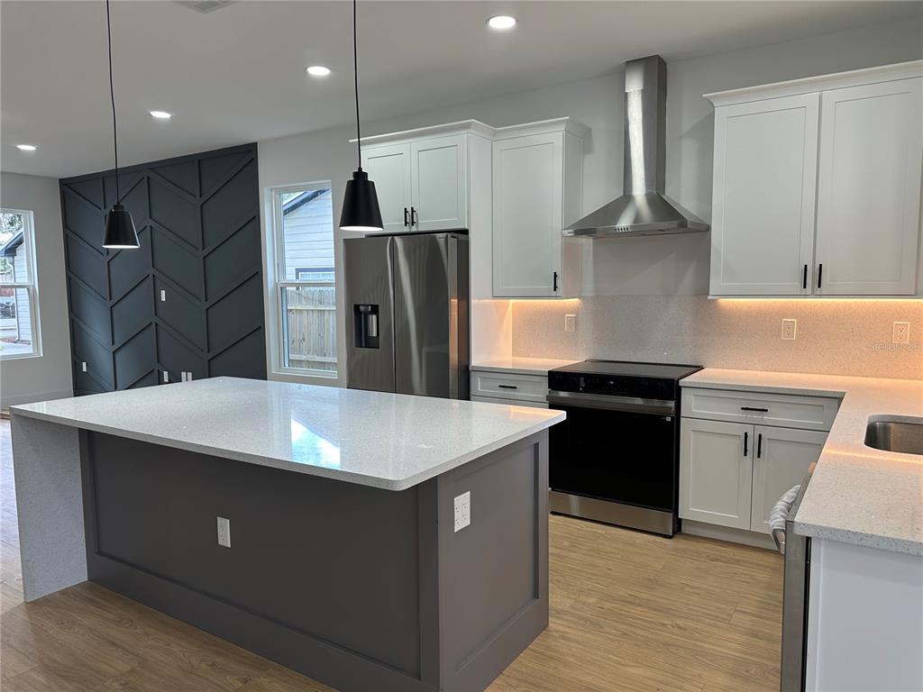 A modern kitchen features a gray island, white cabinetry, stainless steel appliances, and herringbone wall paneling — 1317 E HARDING STREET, ORLANDO, FL