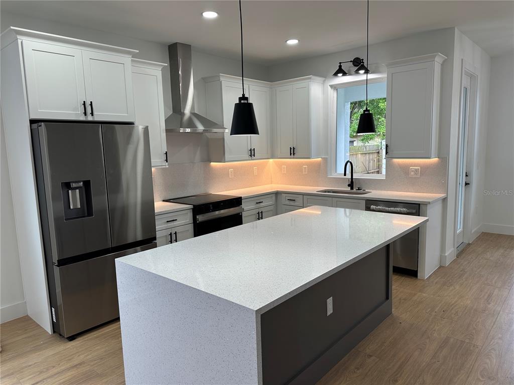 A modern kitchen features white cabinetry, stainless steel appliances, a quartz island, and wood flooring — 1317 E HARDING STREET, ORLANDO, FL