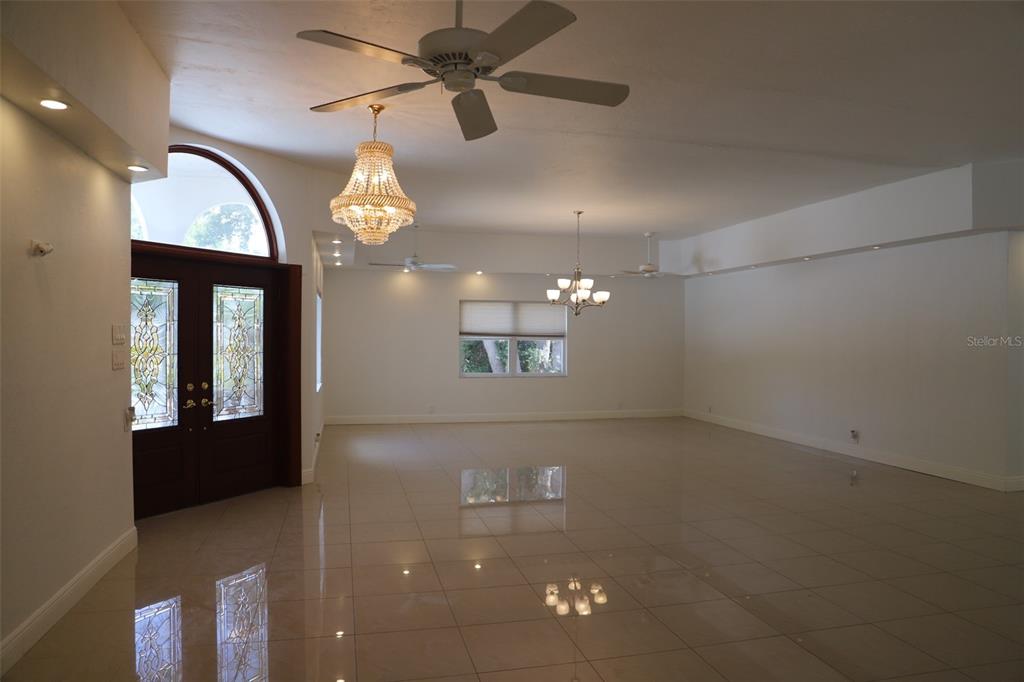 A spacious, empty living room features white walls, tile flooring, a chandelier, and double doors — 2810 61ST STREET, SARASOTA, FL