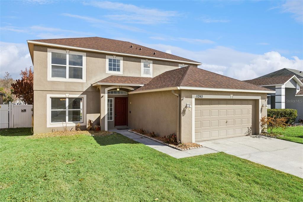 A two-story suburban house features a tan stucco exterior, brown roof, and attached garage — 11245 DACRE LANE, ORLANDO, FL