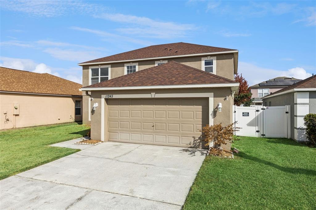 A two-story house with a tan stucco exterior, a brown shingled roof, and a garage — 11245 DACRE LANE, ORLANDO, FL