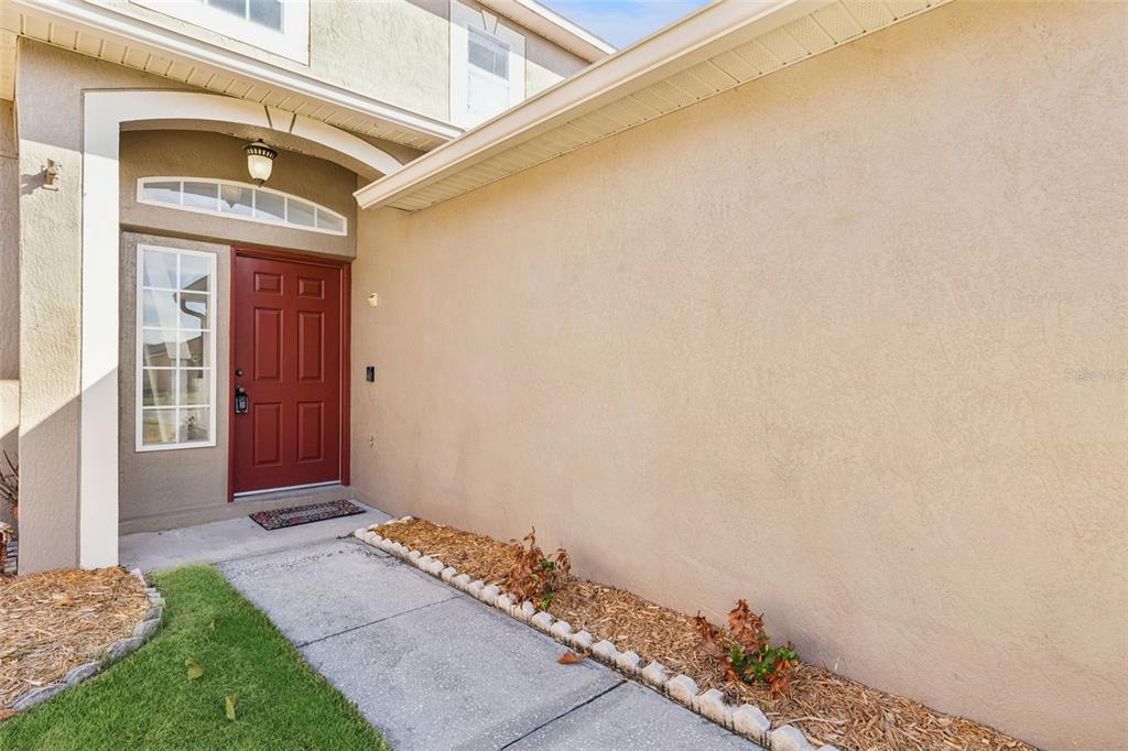 A red front door is set into a tan stucco exterior with a concrete walkway — 11245 DACRE LANE, ORLANDO, FL