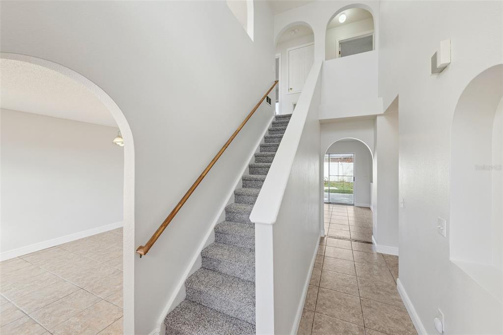 A staircase with gray carpet and a wooden handrail sits in a tiled entryway — 11245 DACRE LANE, ORLANDO, FL