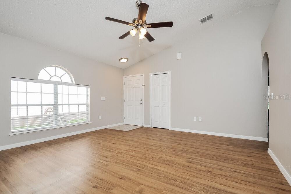 A living room with light gray walls, wood-look flooring, a ceiling fan, and arched window — 30250 RATTANA COURT, WESLEY CHAPEL, FL