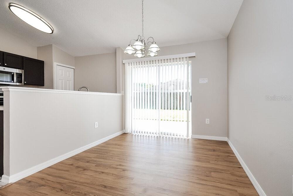 A dining area features light wood-look flooring, a chandelier, and sliding glass doors — 30250 RATTANA COURT, WESLEY CHAPEL, FL