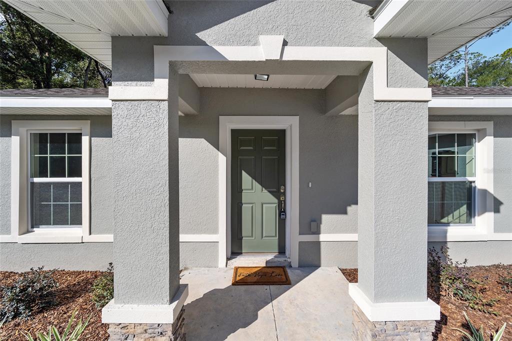 A front entryway with a green door, gray stucco walls, and two large support columns — 2398 W DEVON DRIVE, CITRUS SPRINGS, FL