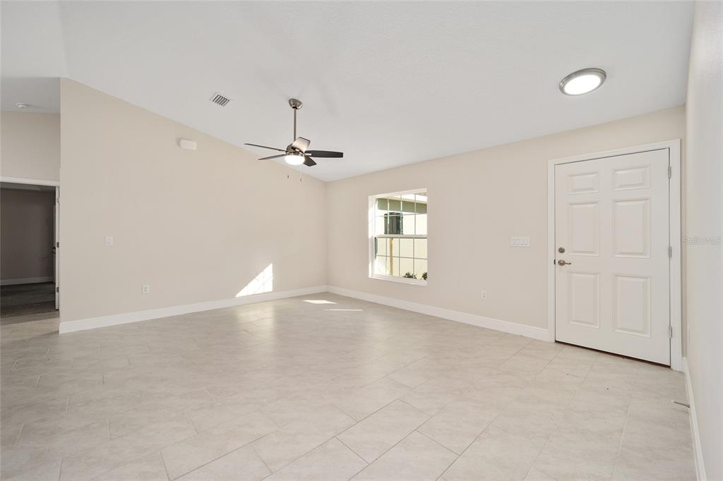 A bright, empty living room features light-colored tile flooring, a ceiling fan, and a front door — 2398 W DEVON DRIVE, CITRUS SPRINGS, FL