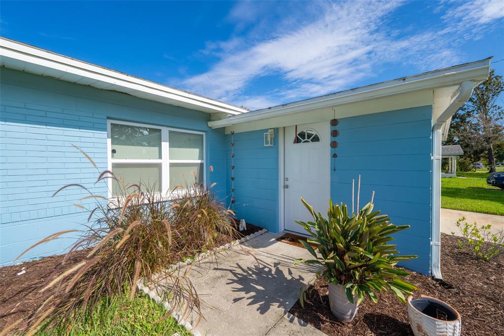 A light blue house exterior features a white front door, a window, and landscaping — 309 3RD STREET, MERRITT ISLAND, FL