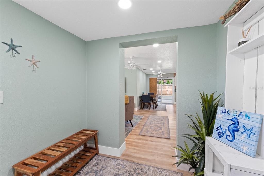 A light green entryway features a wooden bench, coastal decor, and a view into the dining area — 309 3RD STREET, MERRITT ISLAND, FL