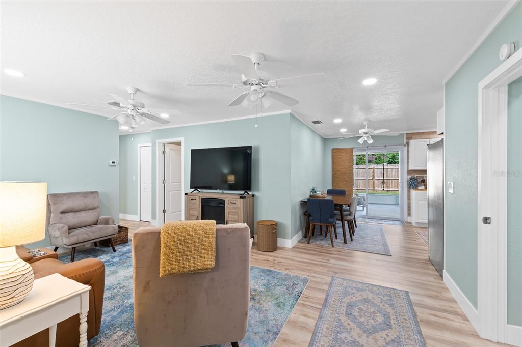An open-concept living and dining area features light blue walls, wood-look flooring, and ceiling fans — 309 3RD STREET, MERRITT ISLAND, FL