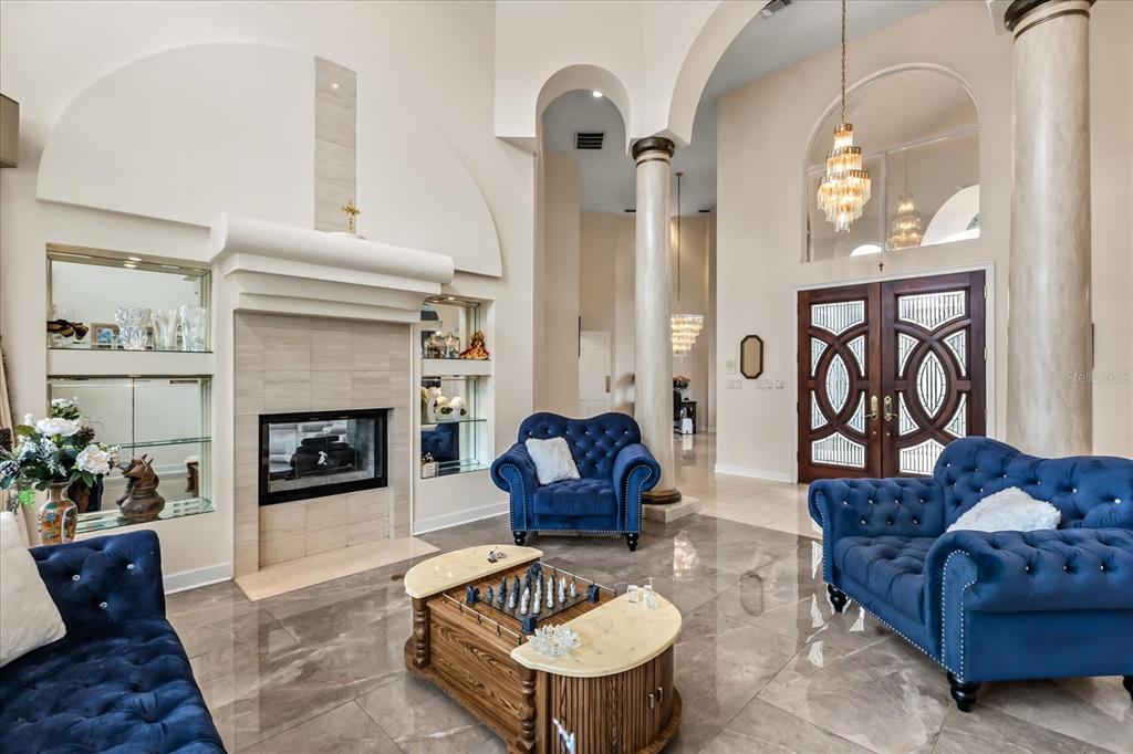 A living room features a fireplace, blue tufted furniture, marble floors, and tall decorative columns — 1036 GOLF VALLEY DRIVE, APOPKA, FL