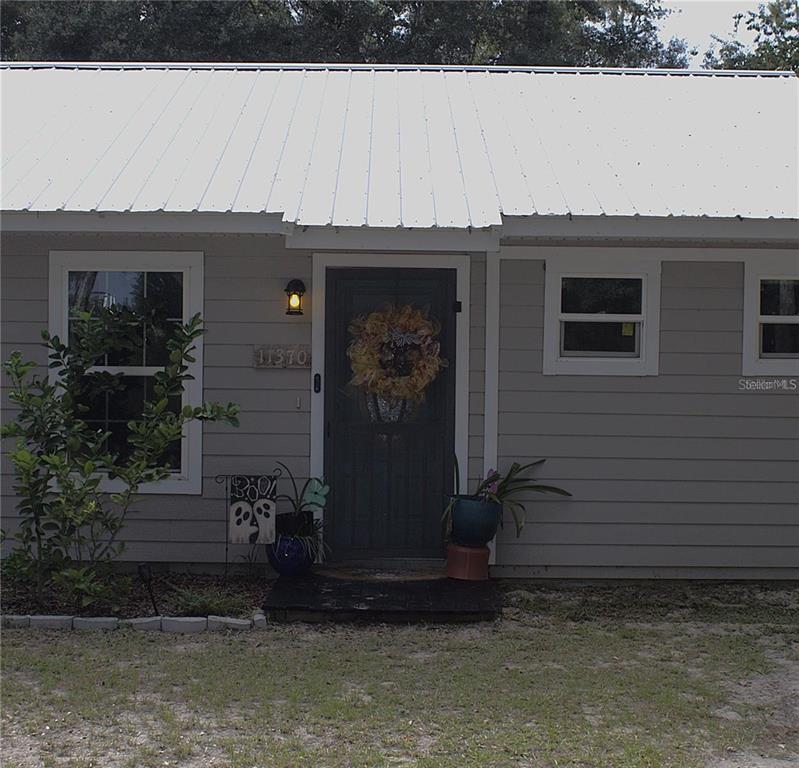 The exterior of a gray house features a white metal roof and a front door — 11370 SW 175TH COURT, DUNNELLON, FL
