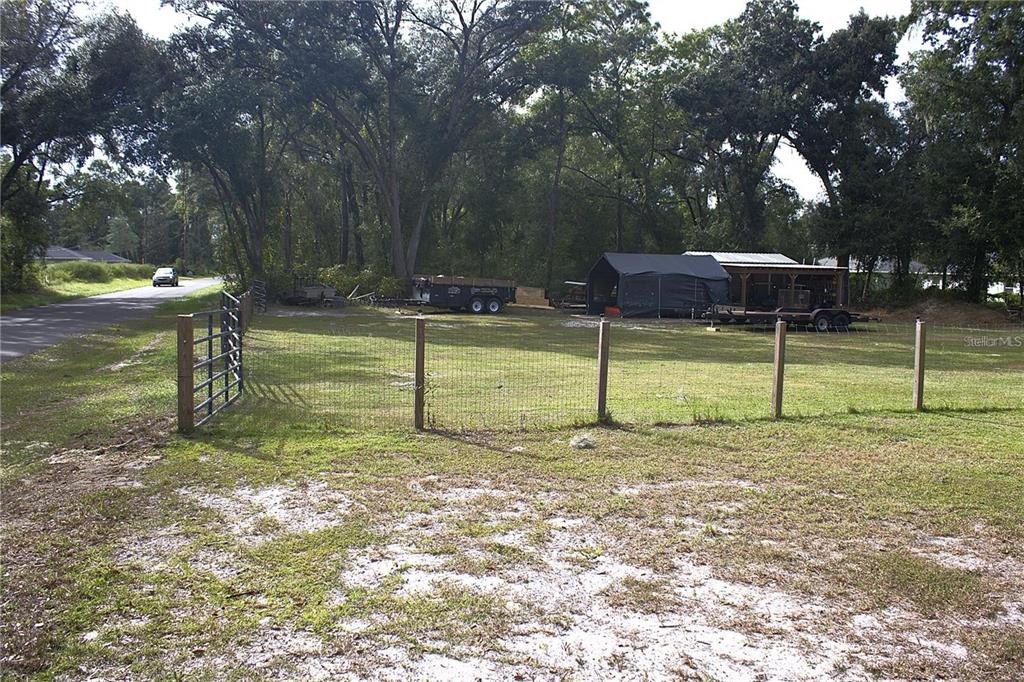 A fenced grassy lot features a metal carport, a trailer, and mature trees — 11370 SW 175TH COURT, DUNNELLON, FL