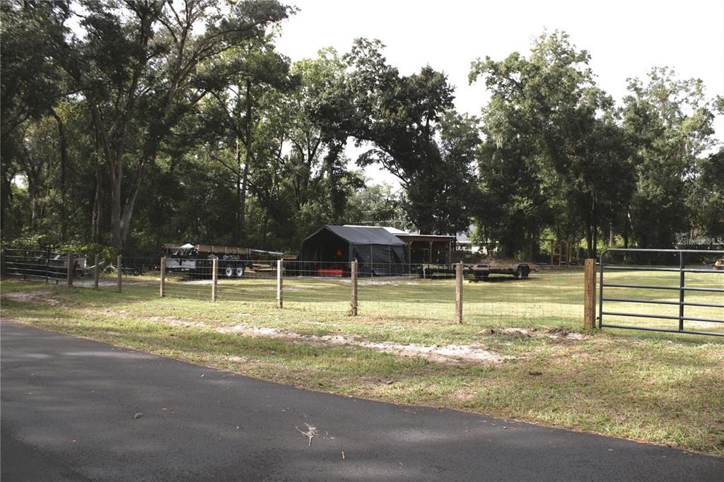 A fenced grassy lot features a portable garage structure and trailers under mature trees — 11370 SW 175TH COURT, DUNNELLON, FL