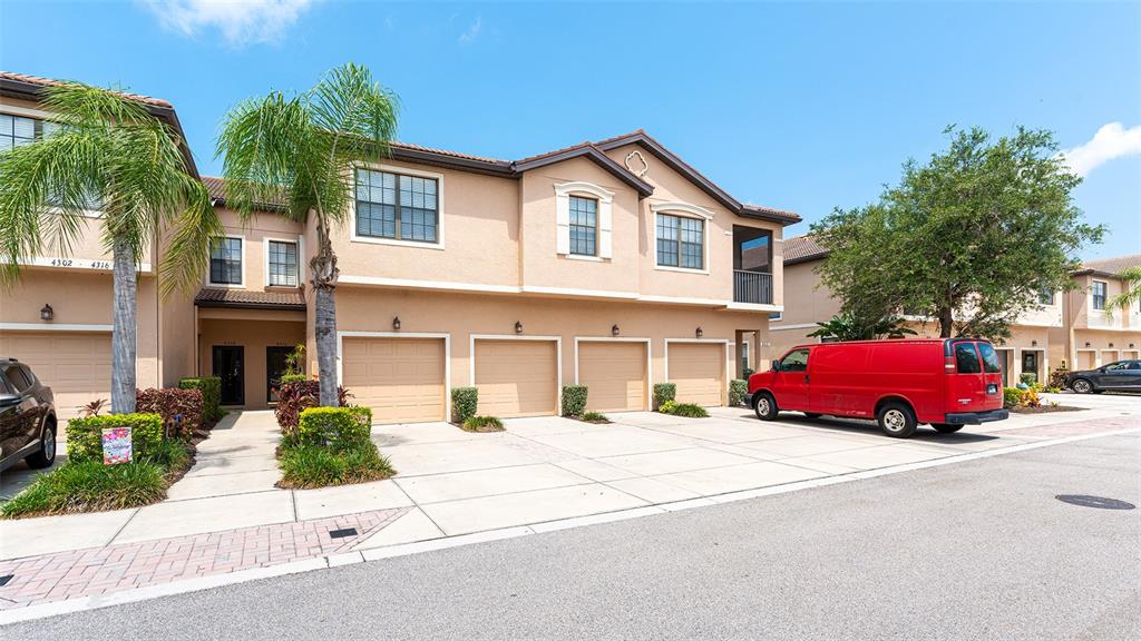 A tan multi-unit townhouse building features four garage doors and a red van parked outside — 4316 VIA PIEDRA CIRCLE UNIT 5-204, SARASOTA, FL