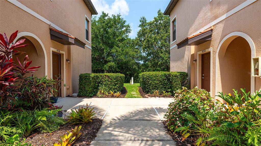 A concrete walkway leads between two tan stucco buildings with arched entryways and lush landscaping — 4316 VIA PIEDRA CIRCLE UNIT 5-204, SARASOTA, FL