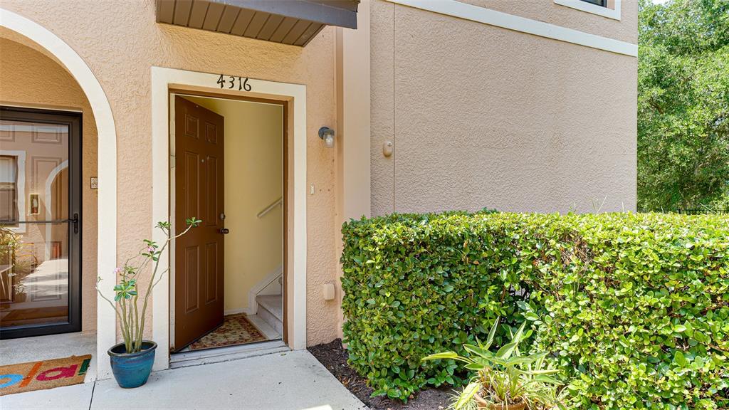 An open brown front door reveals an interior staircase next to a manicured green hedge — 4316 VIA PIEDRA CIRCLE UNIT 5-204, SARASOTA, FL