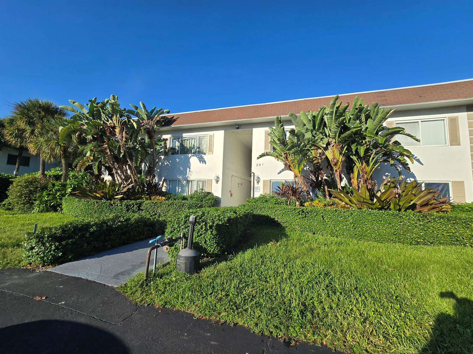 A two-story apartment building exterior features white walls, a brown roof, and lush landscaping — 201 SE 6th Avenue # 16, Pompano Beach FL 33060, POMPANO BEACH, FL