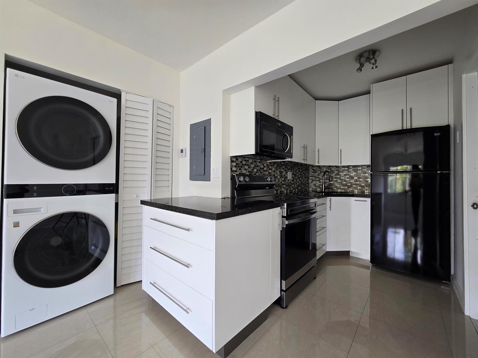 A kitchen features white cabinets, black appliances, a stacked washer-dryer unit, and tile flooring — 201 SE 6th Avenue # 16, Pompano Beach FL 33060, POMPANO BEACH, FL